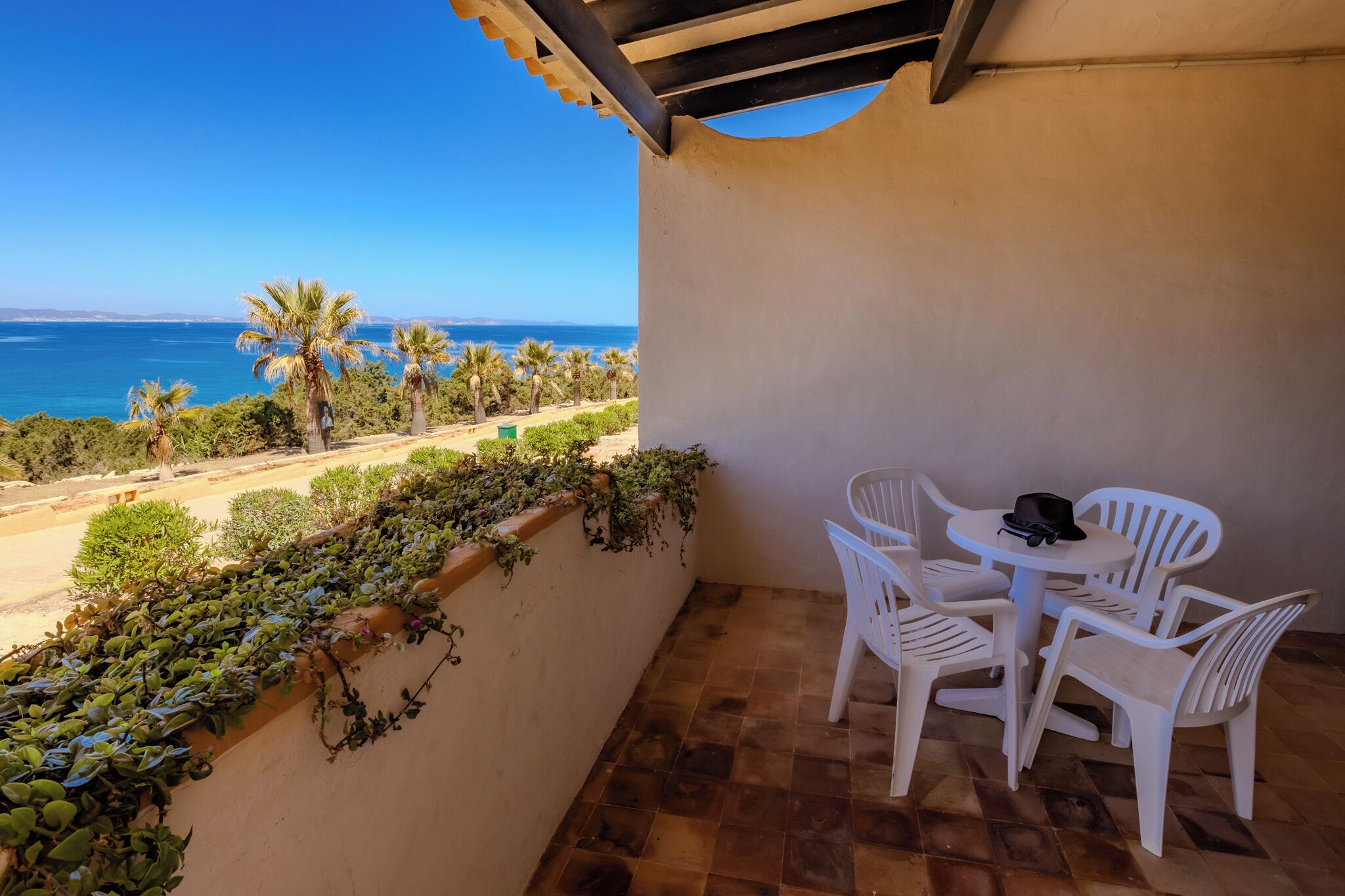 Un balcon avec vue sur la mer, des chaises en plastique blanc et une table.