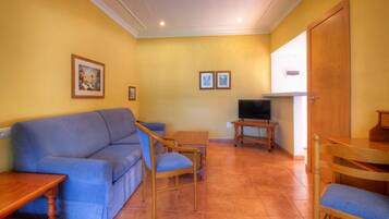 A living room with a blue sofa, wooden chairs, a TV, and two framed pictures on the wall.