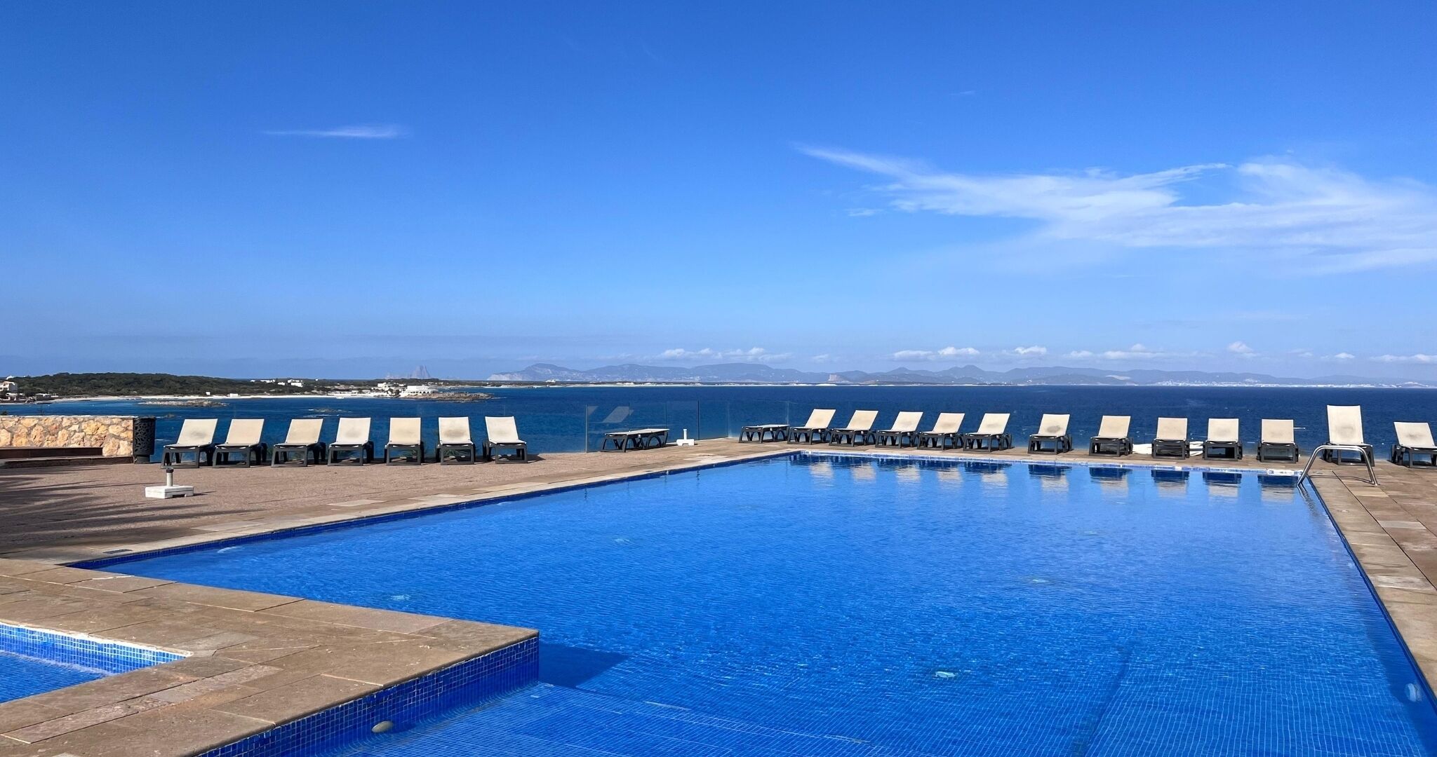 A swimming pool with lounge chairs and a view of the sea.
