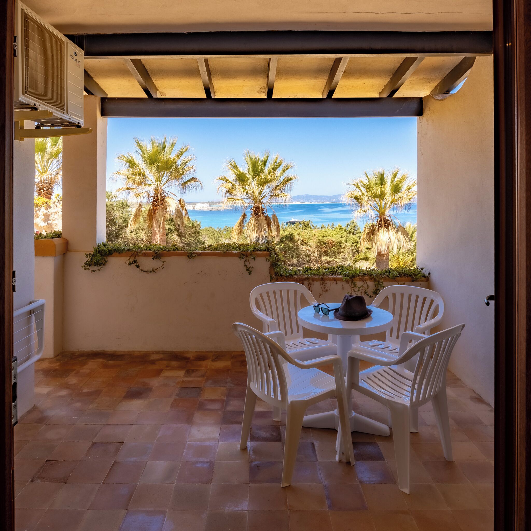 A patio with a table and chairs, a view of the sea, and palm trees.