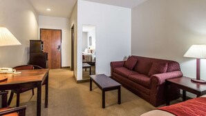 A hotel room with a wooden desk, a red sofa, a small table, and a lamp. - Quality Inn & Suites Guymon East (Guymon)