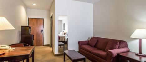 Una habitación de hotel con un escritorio de madera, un sofá rojo, una mesita y una lámpara.
