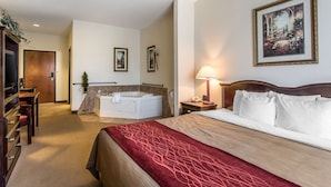 A hotel room with a large bed, a sitting area with a desk and chair, a bathtub, and a framed picture on the wall. - Quality Inn & Suites Guymon East (Guymon)