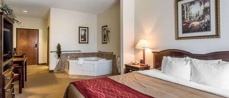 A hotel room with a large bed, a sitting area with a desk and chair, a bathtub, and a framed picture on the wall.