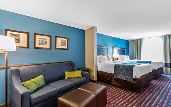 Habitación de hotel con pared azul, sofá con cojines amarillos, cama con ropa de cama blanca y alfombra estampada.