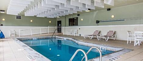 An indoor swimming pool with clear water, a diving board, and lounge chairs along the poolside.