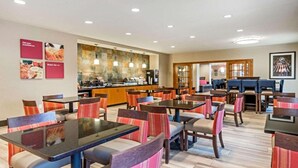 A hotel dining area with multiple tables and chairs, a kitchen in the background, and a bar area. - Comfort Suites Fairview Heights - St. Louis (Fairview Heights)