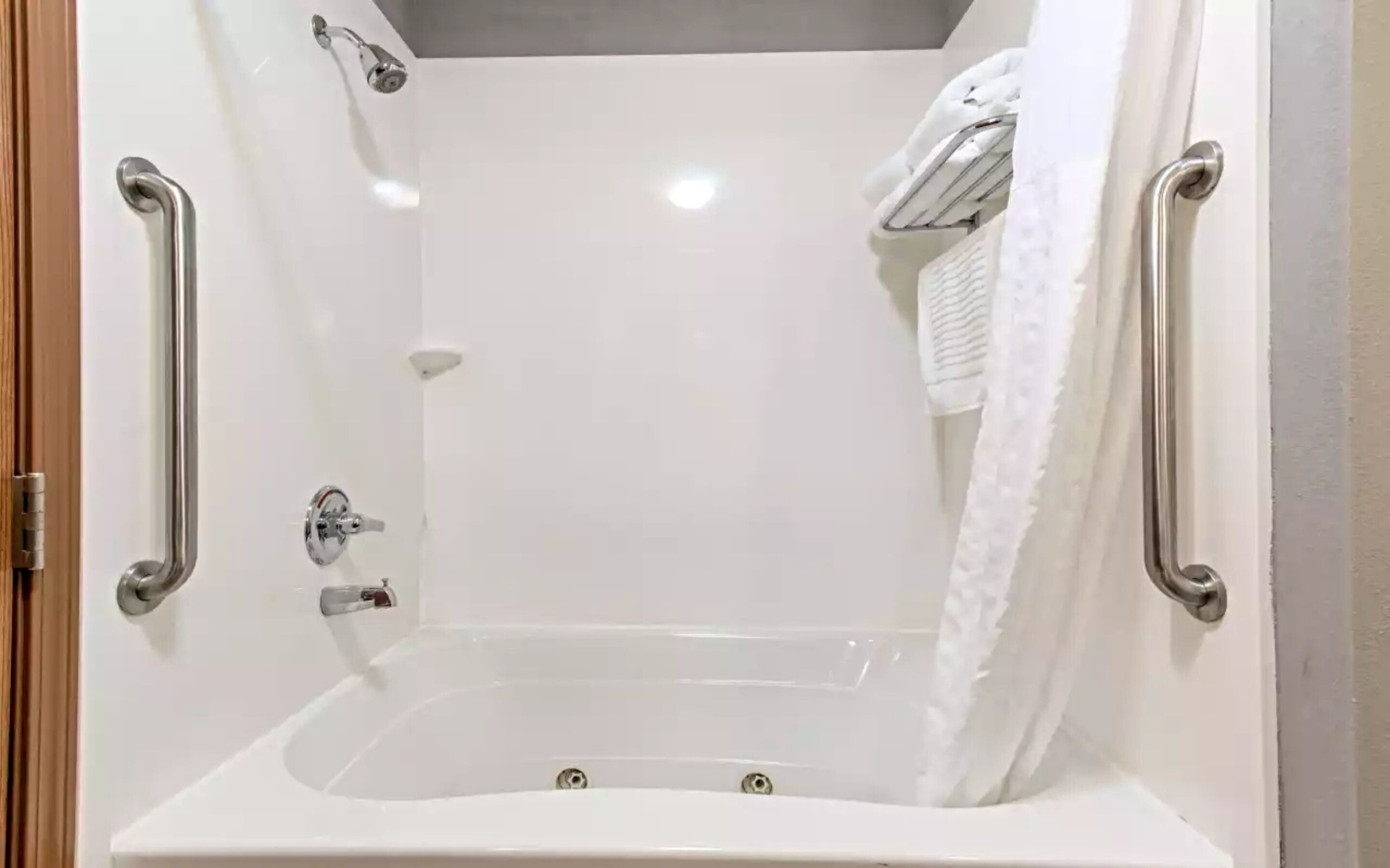 A white, walk-in shower with a bathtub, grab bars, and a towel rack.