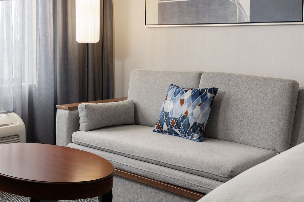 A modern living room with a grey sofa, a wooden coffee table, and a patterned throw pillow.