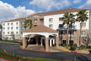 Un hotel Courtyard by Marriott con entrada cubierta, palmeras y aparcamiento.
