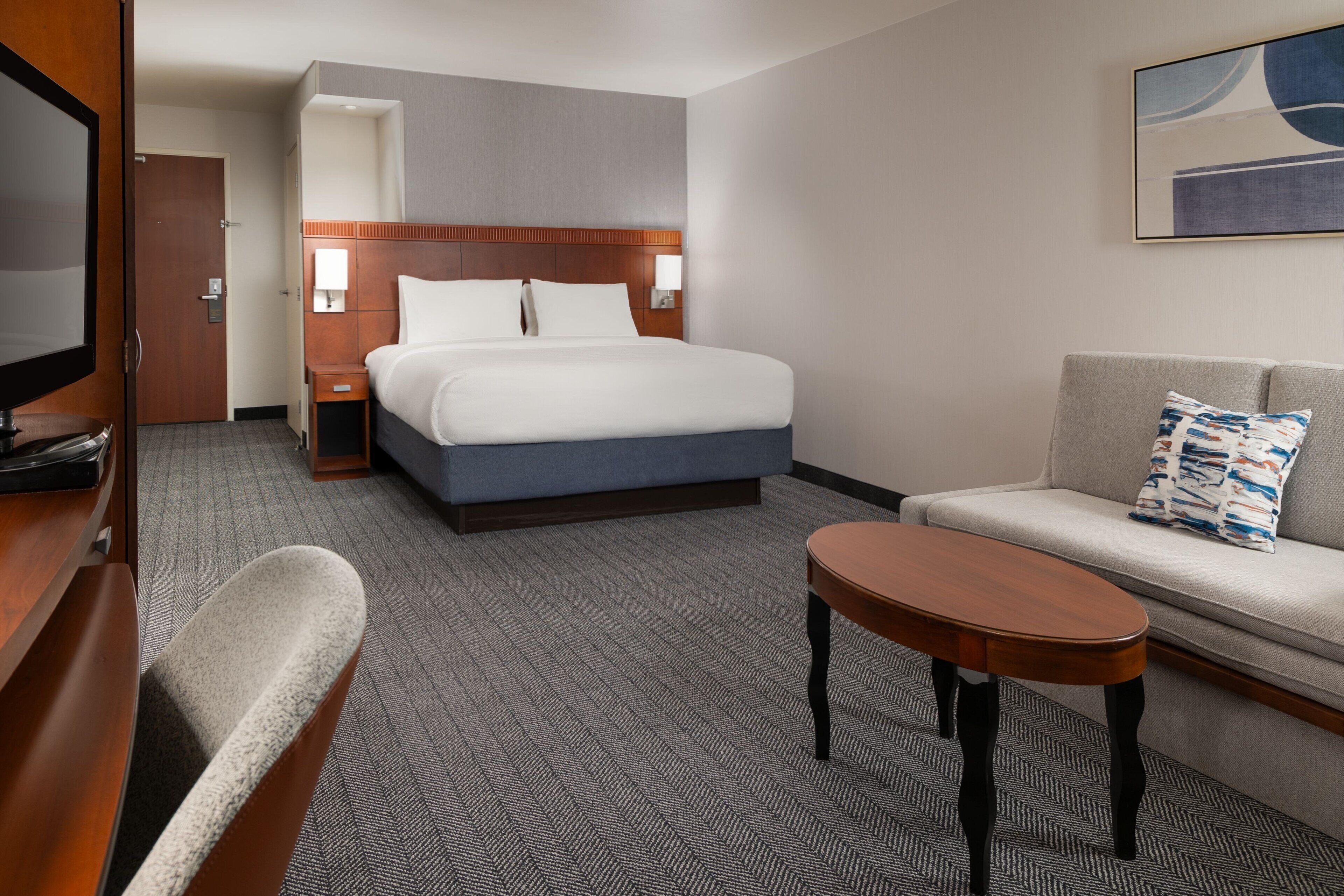 A hotel room with a bed, a sofa, a small table, a TV, and a door.