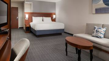 A hotel room with a bed, a sofa, a small table, a TV, and a door.