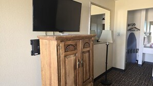 Une chambre d’hôtel équipée d’un meuble en bois, d’un téléviseur à écran plat, d’un miroir, d’une lampe et d’un porte-serviettes.
