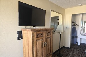 A hotel room with a wooden cabinet, a flat-screen TV, a mirror, a lamp, and a towel rack. - Econo Lodge Eagle Nest (Eagle Nest)