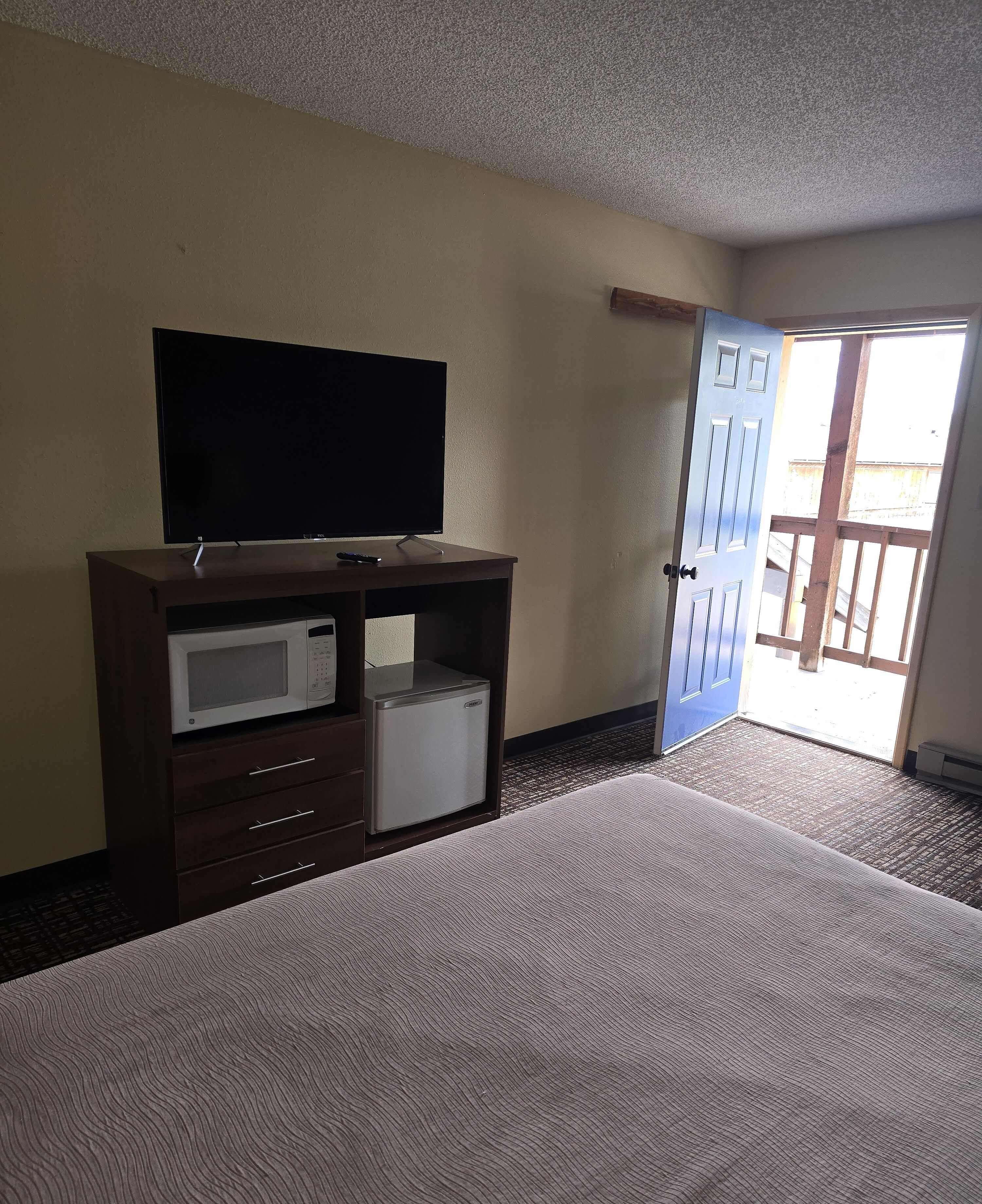 Een hotelkamer met een bed, een televisie op een houten kast, een magnetron en een deur naar een balkon.