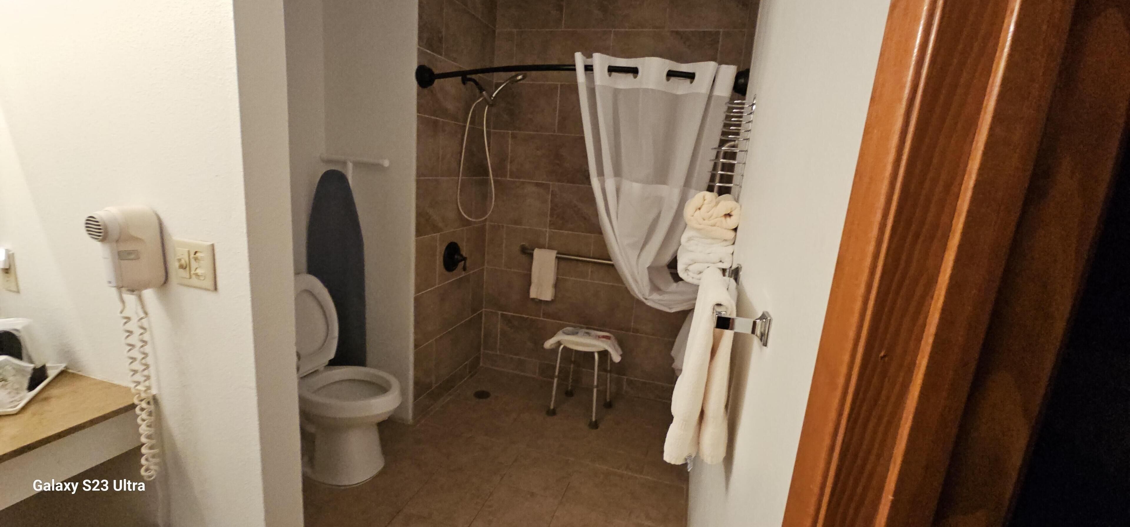 Une salle de bain comprenant des toilettes, une douche avec un rideau, un porte-serviettes avec des serviettes et un sèche-cheveux fixé au mur.