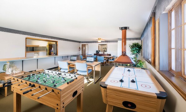 A room with a foosball table, shuffleboard table, and a bar area with stools.