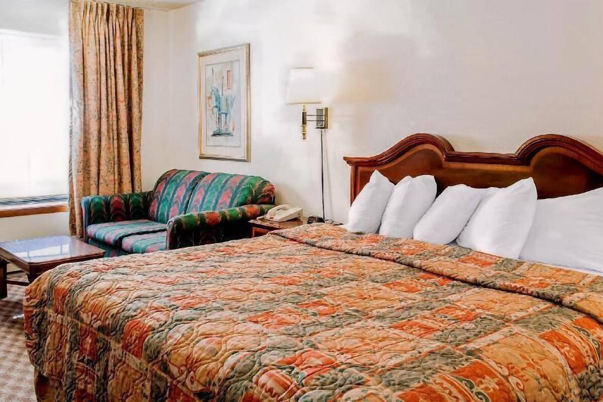 Quarto de hotel com uma cama, uma cadeira, um abajur e um quadro na parede.
