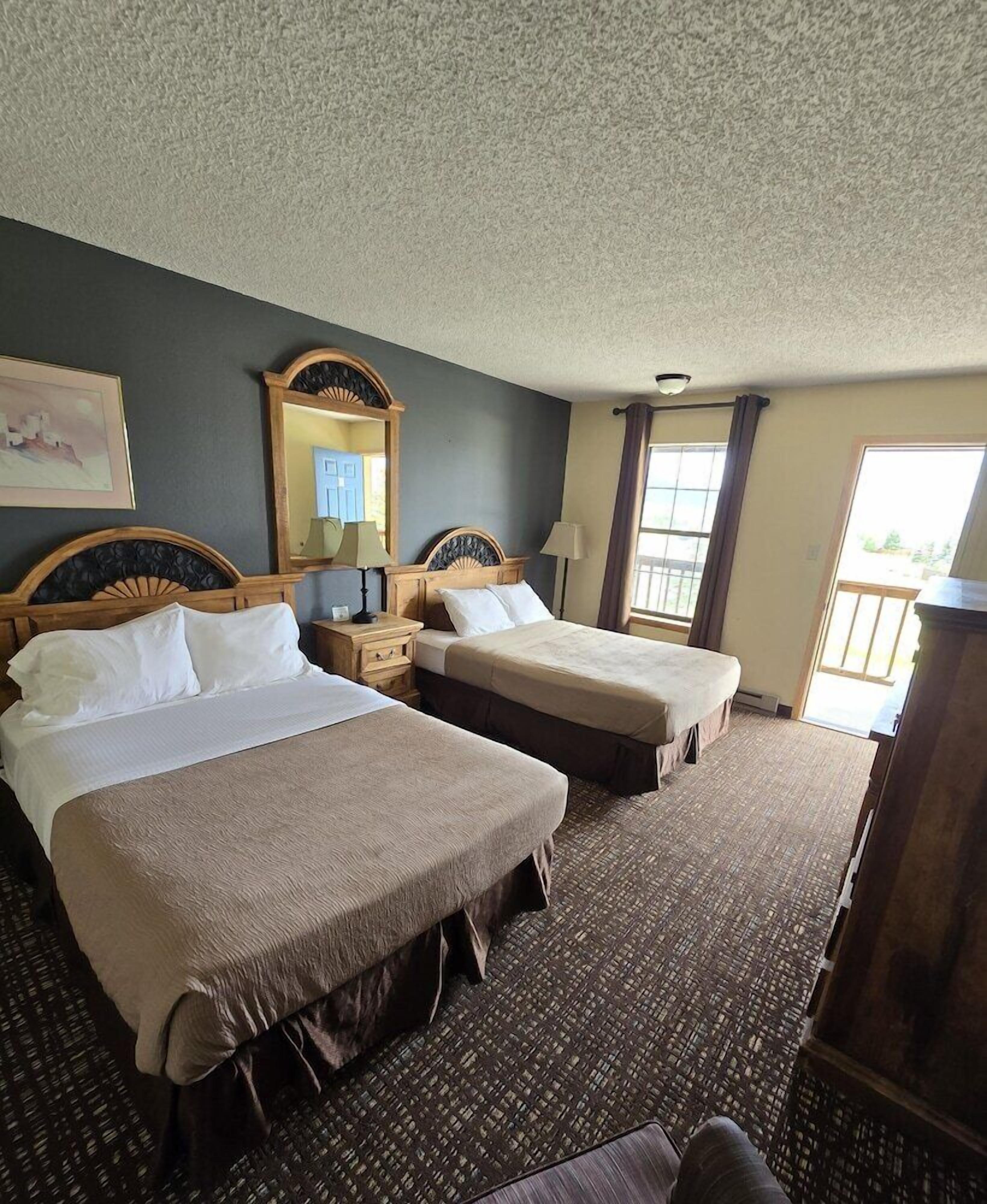 A hotel room with two beds, a large mirror, a window with curtains, and a view of the outdoors.
