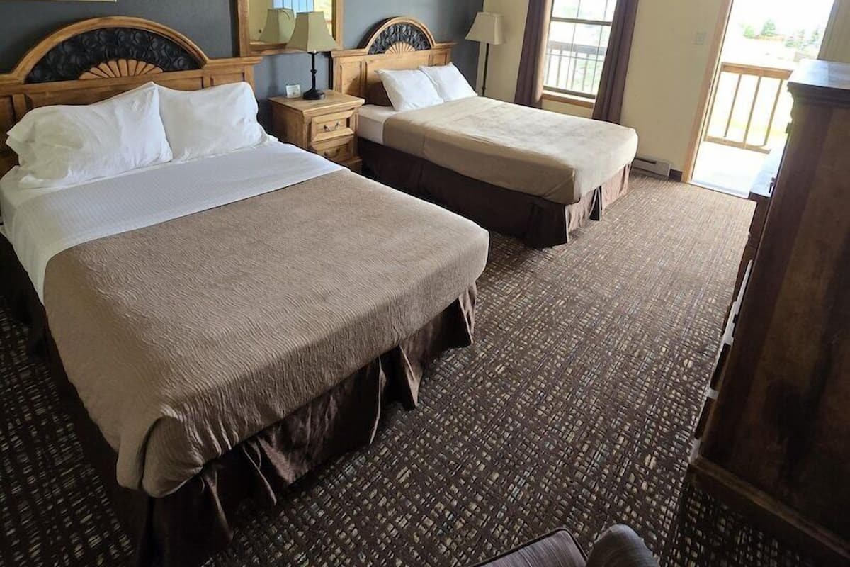 A hotel room with two beds, a large mirror, a window with curtains, and a view of the outdoors.
