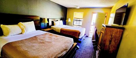 A hotel room with two beds, a wooden dresser, a television, and a window with blinds.