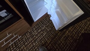 Une chambre d’hôtel avec un téléviseur posé sur un meuble en bois, une télécommande et un réfrigérateur ouvert.