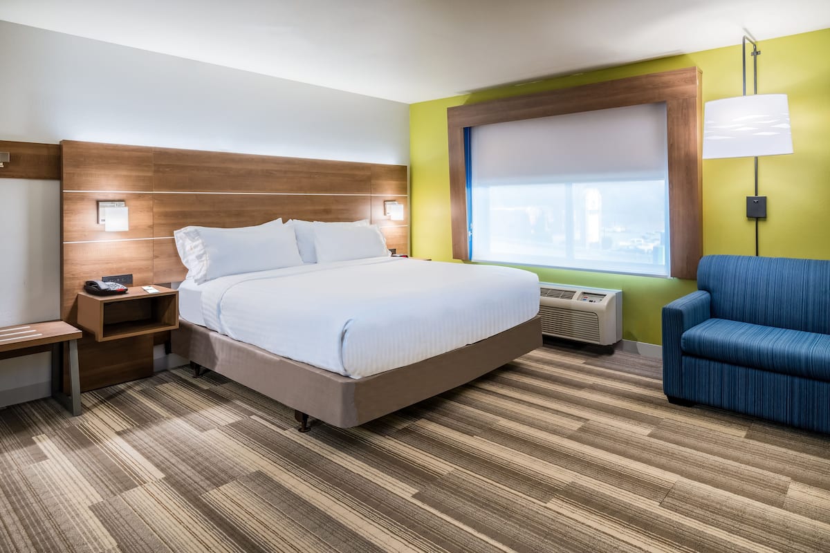 Habitación de hotel con una cama grande, mesita de noche, lámpara y vistas a la ciudad desde la ventana.