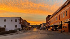 Vista de la calle al atardecer con edificios a ambos lados, cielo despejado y un coche circulando por la carretera.