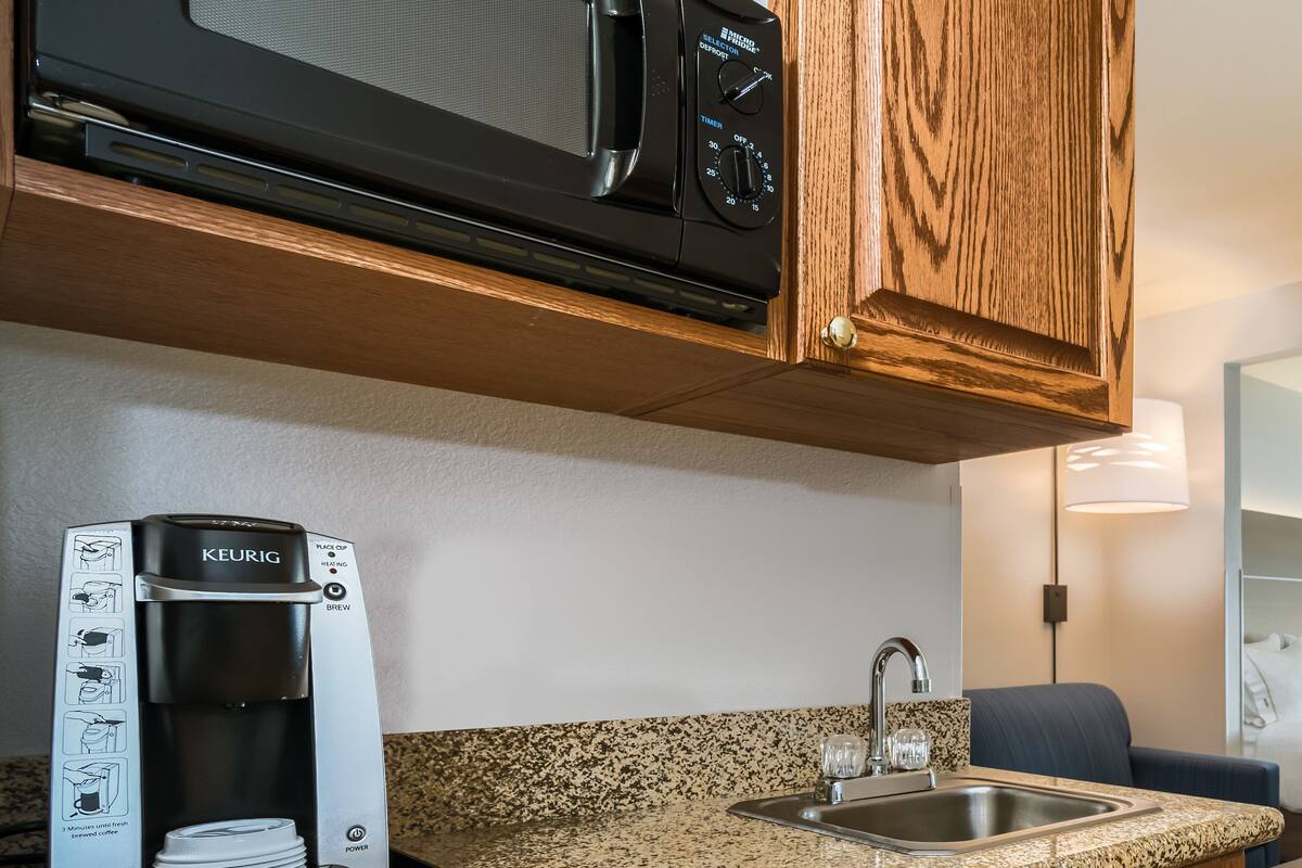 Una kitchenette compacta con microondas, cafetera y lavabo.