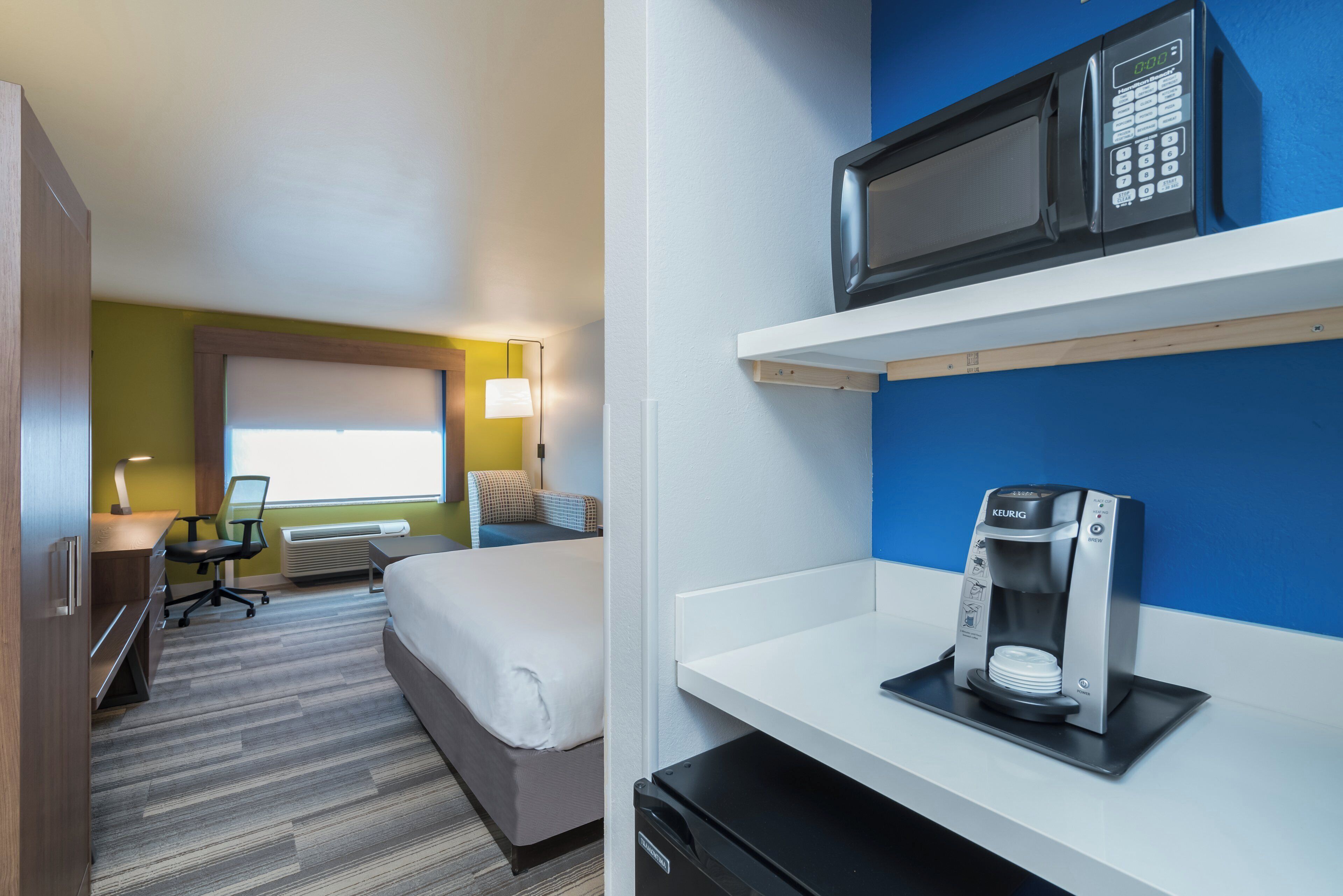 Une chambre d’hôtel avec un lit, un bureau, une chaise et un four à micro-ondes posé sur une étagère.