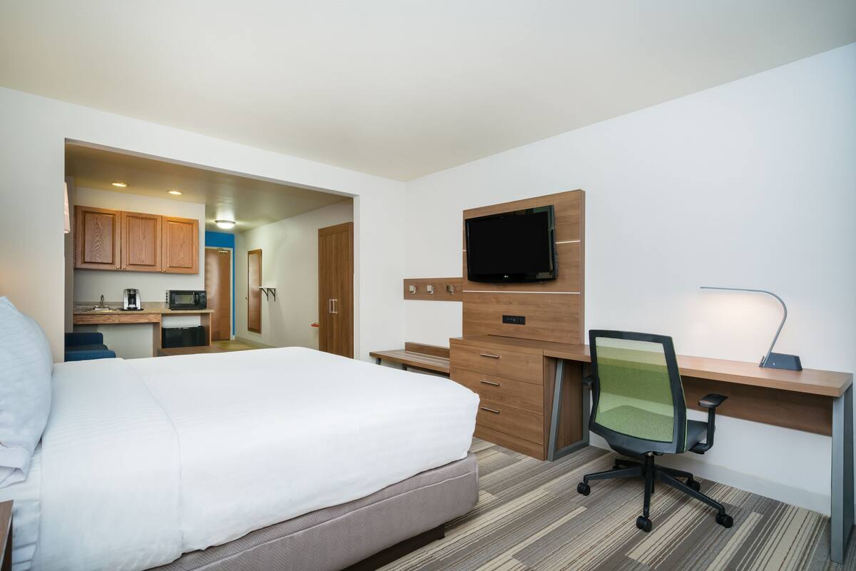 Una habitación de hotel con cama, escritorio con computadora, televisor y kitchenette.