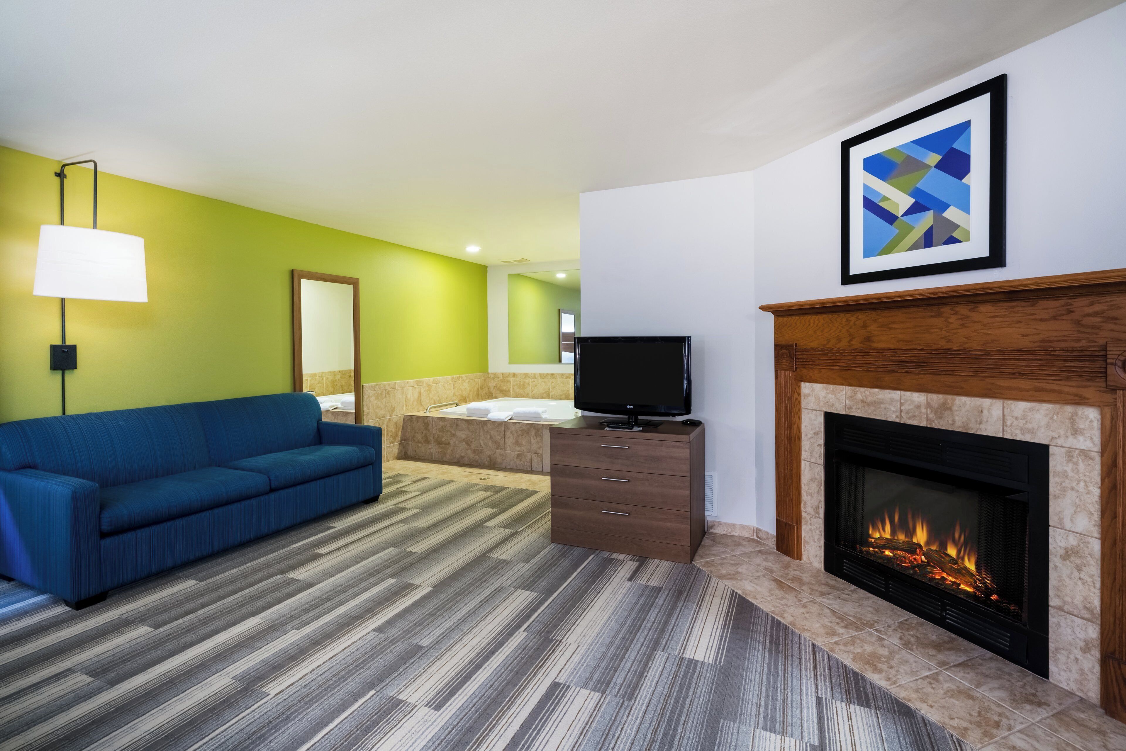 Een hotelkamer met een blauwe bank, een flatscreen televisie, een open haard en een grote spiegel.