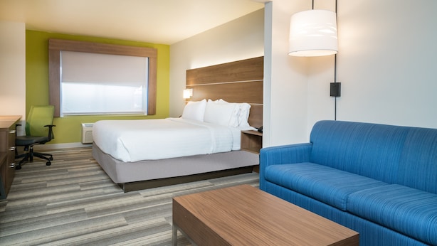 Habitación de hotel con cama, sofá azul, mesa de centro de madera, escritorio con silla y lámpara de pared.