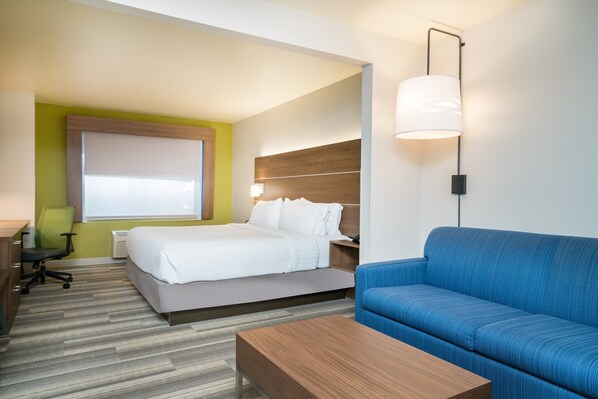 Une chambre d’hôtel avec un lit, un canapé bleu, une table basse en bois, un bureau avec une chaise et une lampe fixée au mur.