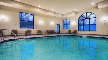 Ein Swimmingpool mit klarem, blauem Wasser, umgeben von Liegestühlen und einem überdachten Bereich mit großen Fenstern.