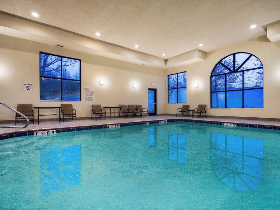 A swimming pool with clear blue water, surrounded by lounge chairs and a sunroofed area with large windows.