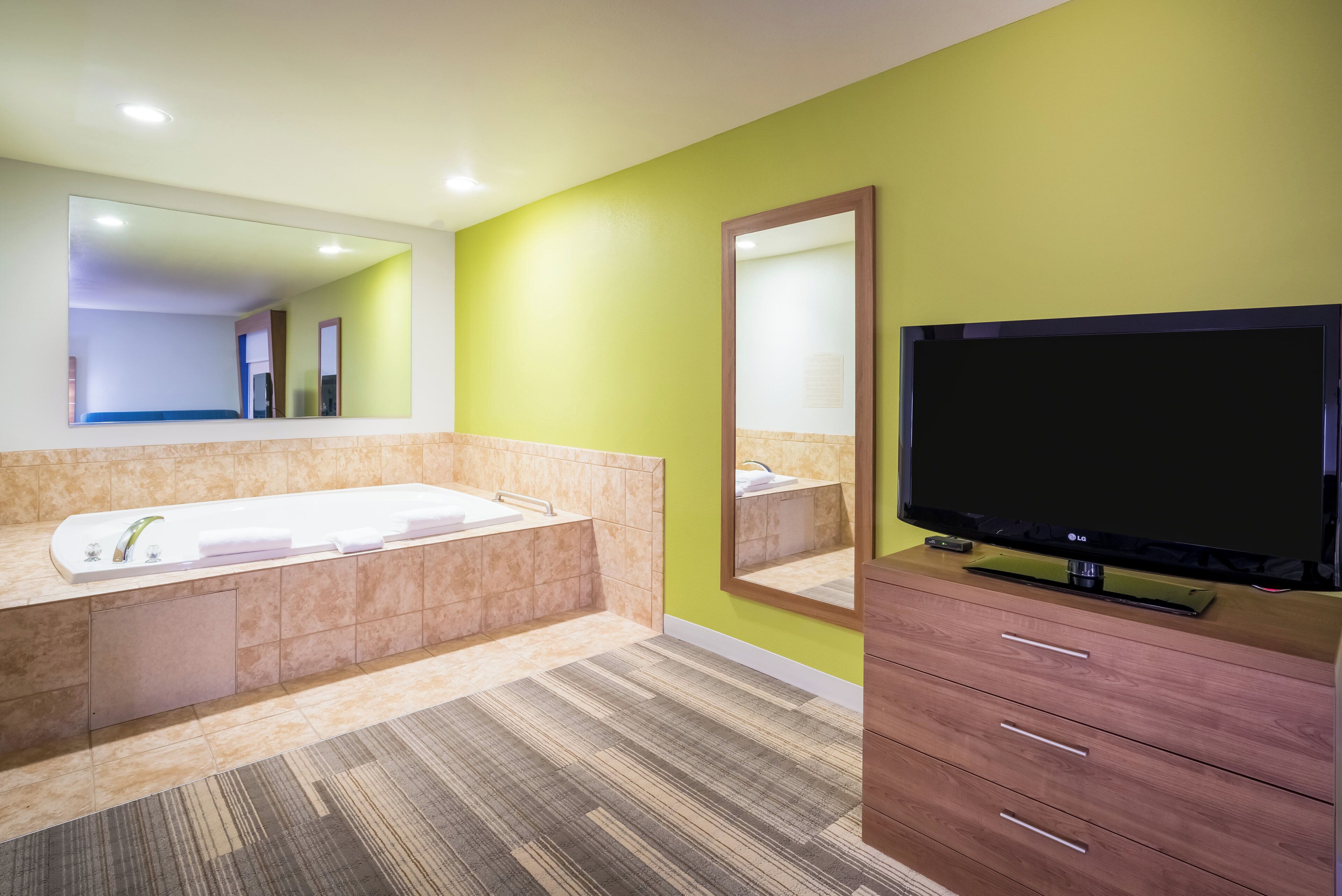 Un baño moderno con bañera, un espejo grande, un televisor y un armario de madera.