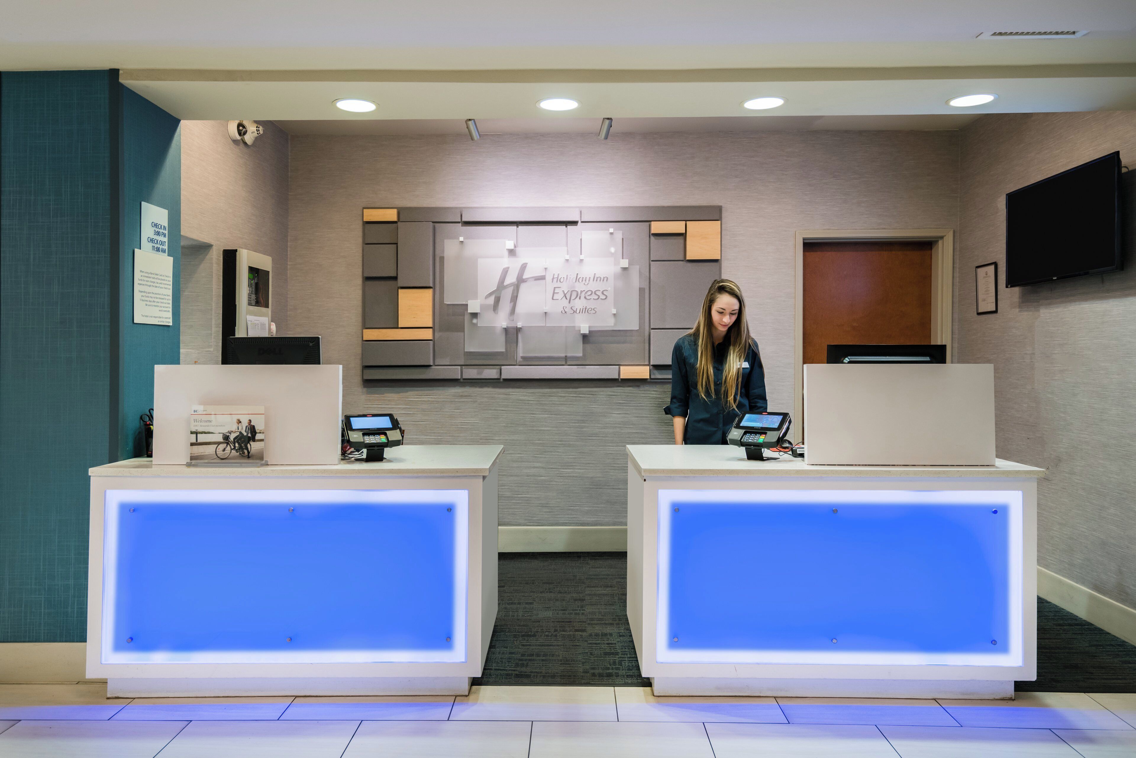 Una recepción de hotel con una pantalla digital, un letrero de Holiday Inn Express Suites y una cámara de seguridad.