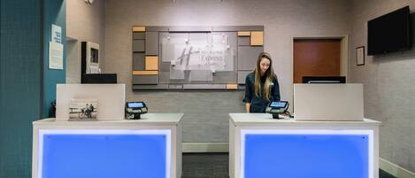 Una recepción de hotel con una pantalla digital, un letrero de Holiday Inn Express Suites y una cámara de seguridad.