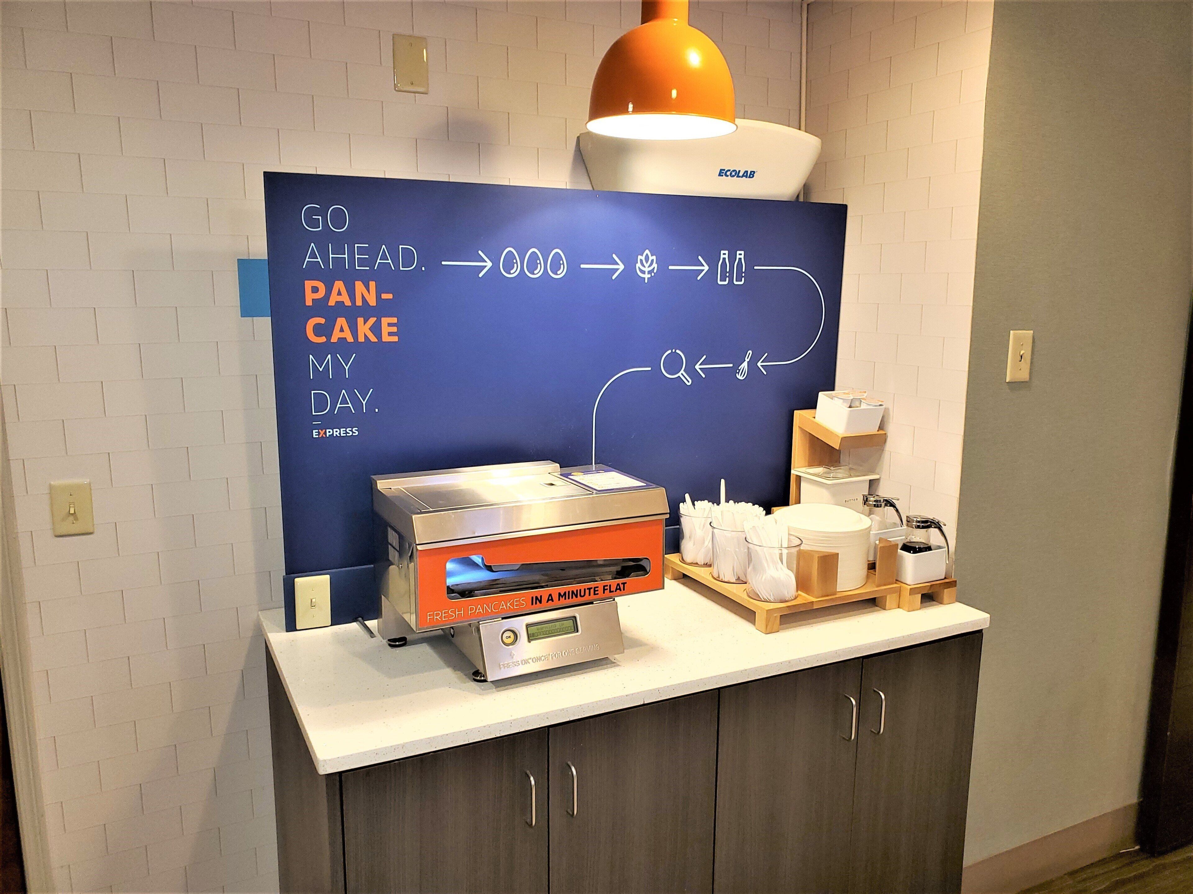 A kitchen area with a flat-top griddle, a sign with a pancake recipe, and a coffee station.