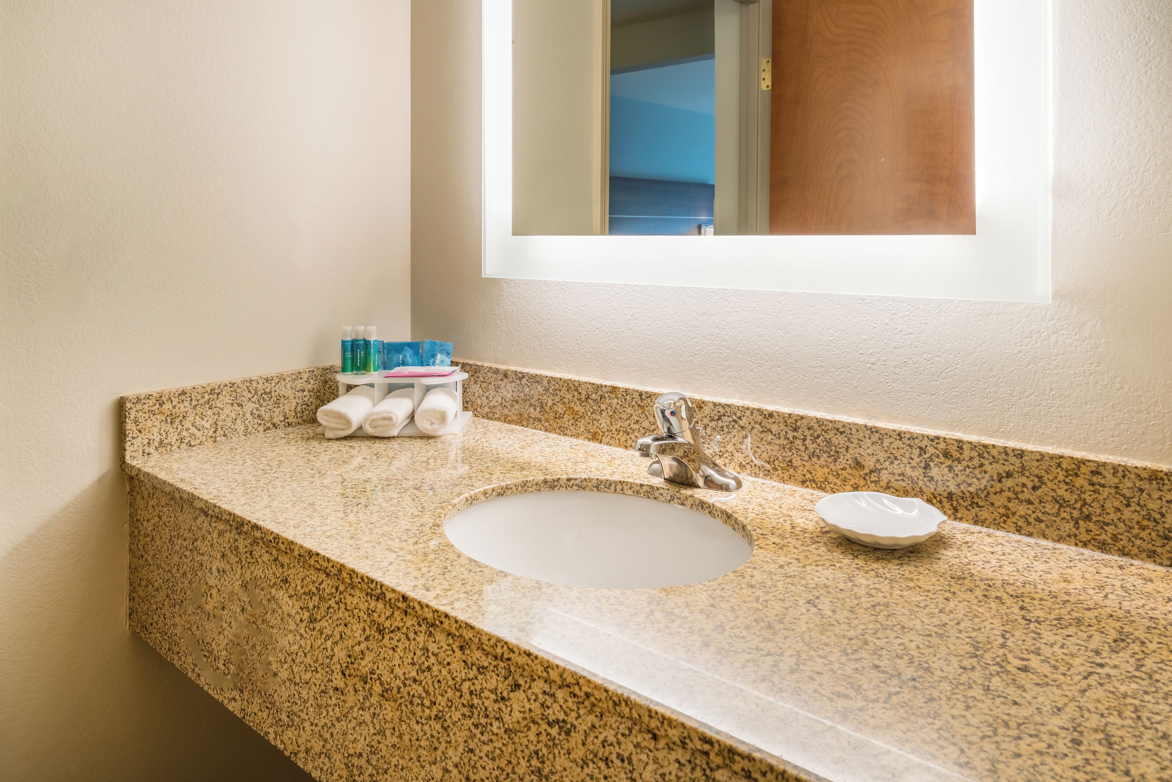 Un baño con encimera de granito, un lavabo blanco y un espejo encima.