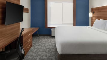 Habitación de hotel con cama, escritorio con silla, televisor de pantalla plana, ventana y aire acondicionado instalado en la pared.