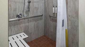 Un espace douche équipé d’un pommeau de douche, de barres d’appui et d’un rideau de douche blanc.