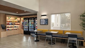 A modern indoor seating area with tables and chairs, a vending machine, and a snack display. - City Express By Marriott Rancho Cucamonga (Rancho Cucamonga)