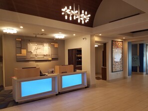 A reception area with a modern design, featuring a reception desk, a wall-mounted information board, and a decorative ceiling light fixture.