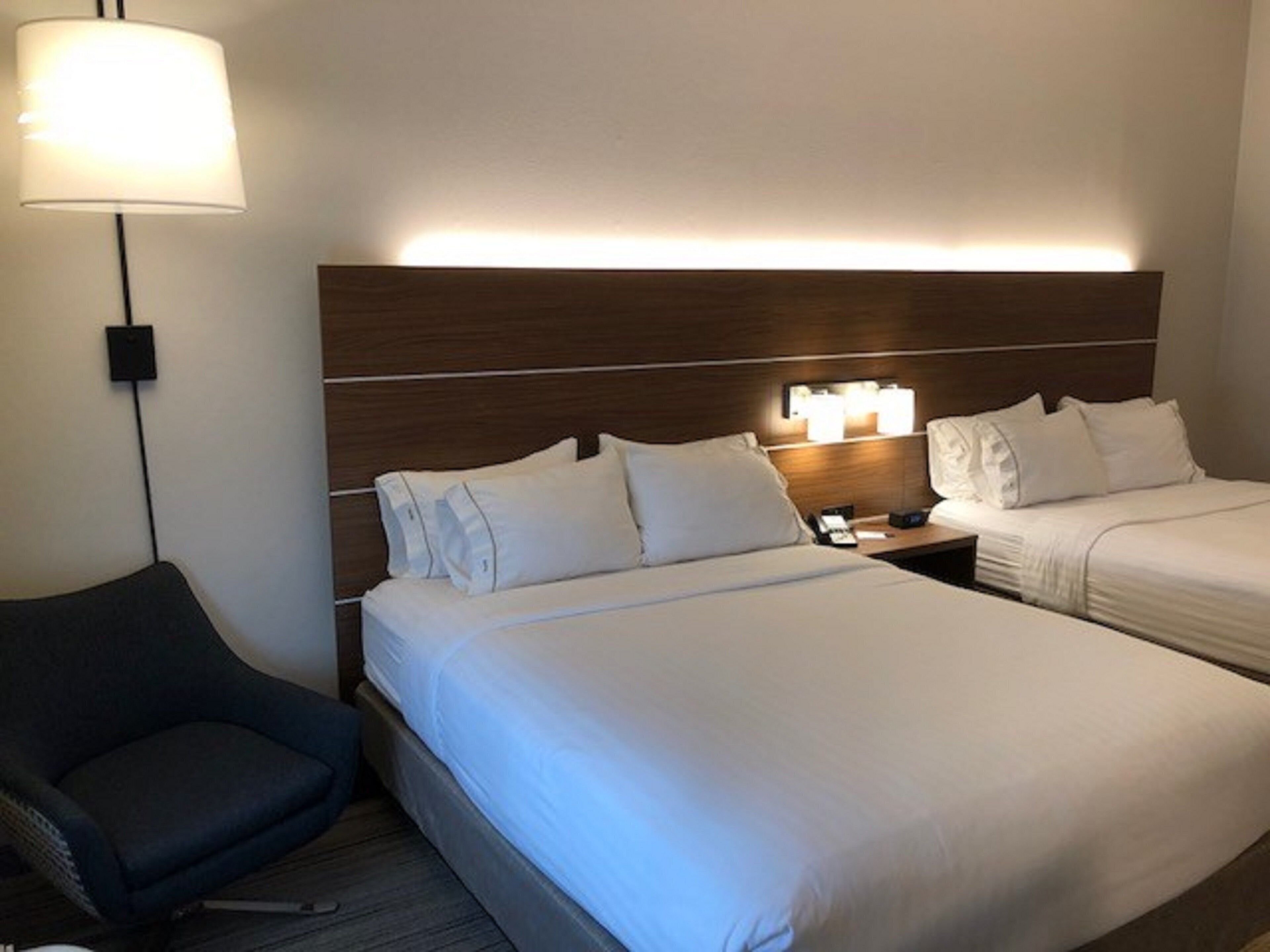 A hotel room with two beds, a nightstand, a lamp, and a chair.