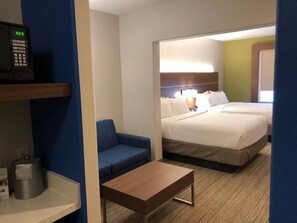 Quarto de hotel com cama, escrivaninha, cadeira e mesa pequena.