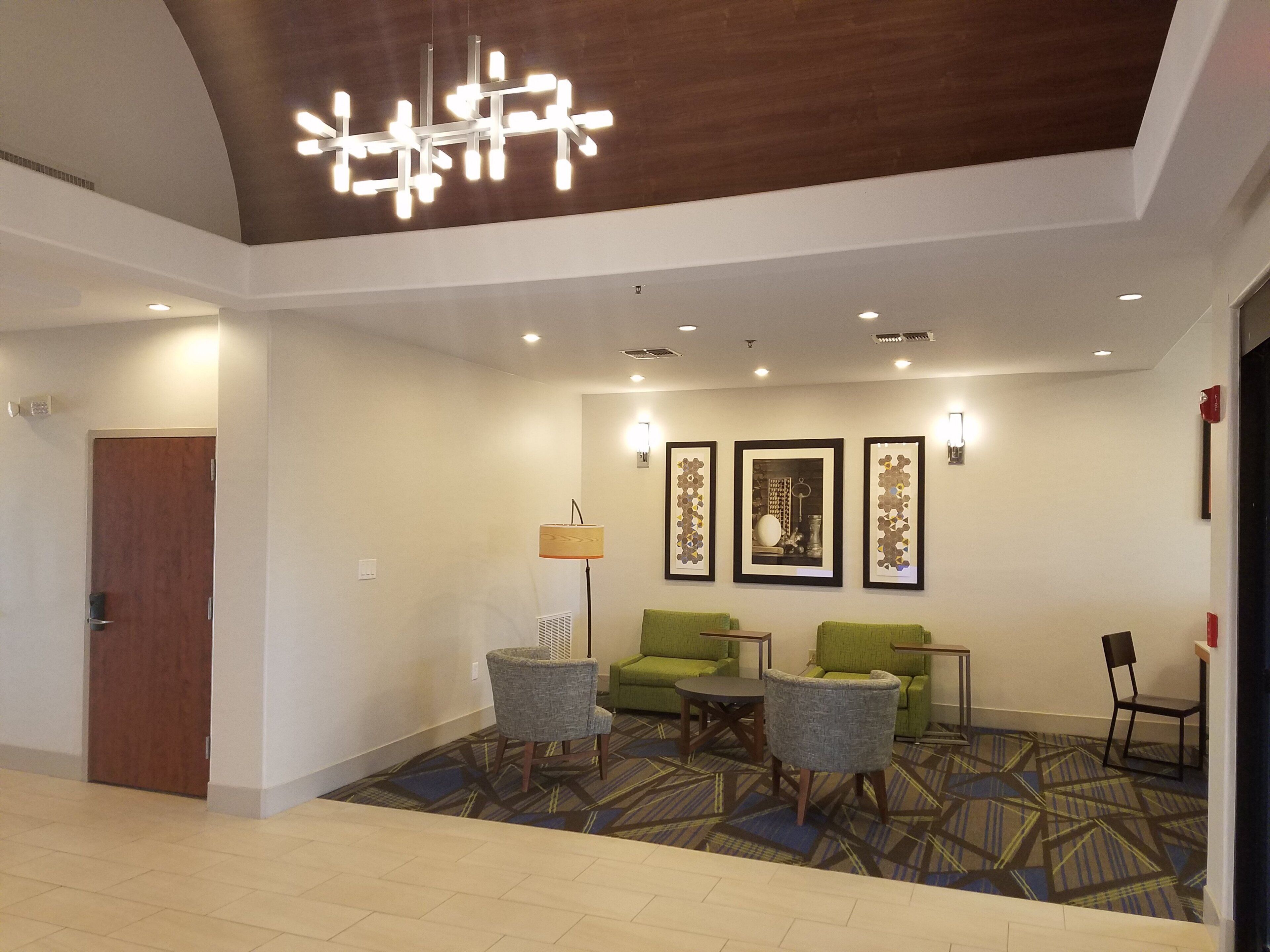 Un vestíbulo de hotel con una lámpara de araña moderna, asientos verdes, obras de arte enmarcadas y una alfombra estampada.