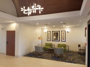 Un hall d’hôtel doté d’un lustre moderne, de sièges verts, d’œuvres d’art encadrées et d’un tapis à motifs.