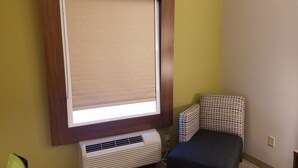 A room with a large window covered by a beige blind, a white air conditioning unit, a patterned chair, and a small table. - Holiday Inn Express & Suites Rio Grand by IHG (Rio Grande City)